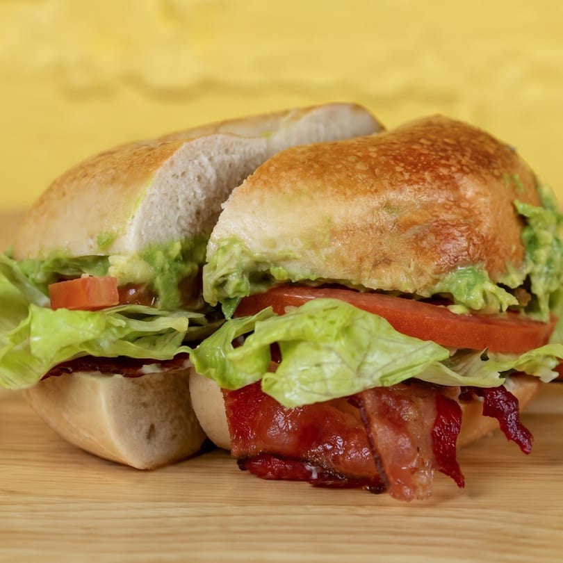 A sliced sandwich with bacon, lettuce, tomato, and avocado spread on a wooden board.